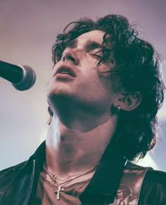 a young man with curly hair and piercings on his neck singing into a microphone