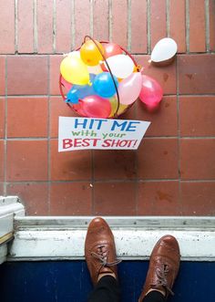 a person's feet with brown shoes and balloons on the side of a brick wall