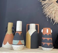 five vases sitting on top of a wooden shelf next to a black bag and straw wreath