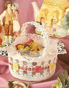 there is a white lace basket with flowers in it and two figurines next to it