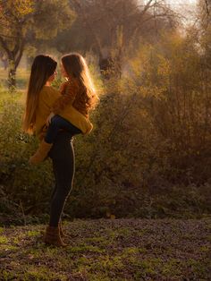 two young women standing in the woods with their backs to each other and looking at each other