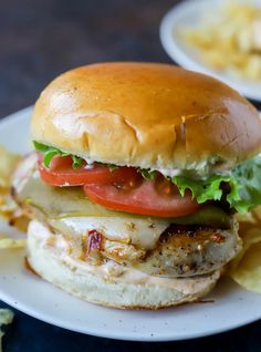 a chicken sandwich with tomatoes, lettuce and cheese on a plate next to chips