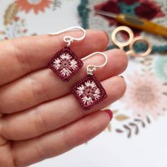 a person is holding two small square earrings in their left hand and scissors on the right