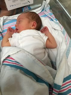 a baby is sleeping on a blanket in a glass case with a white and blue striped blanket