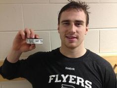 a young man holding up a small clock in front of his face and wearing a t - shirt that says flyers