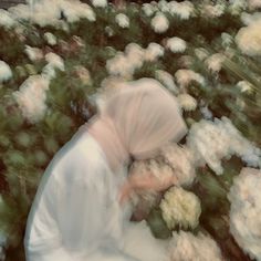 a blurry image of a woman picking flowers from a bed of white and green flowers