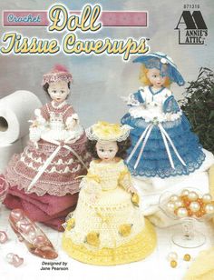 three dolls in dresses and bonnets are sitting next to some rolls of toilet paper