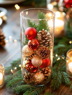 Festive glass vase centerpiece with red and gold baubles, pinecones, and evergreen branches. Surrounded by candles on a wooden table. Cozy holiday ambiance. Cheap Table Decor, Table Decor For Christmas, Christmas Party Centerpieces, Decor Ideas For Christmas, Cheap Table, Christmas Table Centerpieces, Table Decor Ideas, Christmas Entertaining, Decor For Christmas