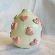 a white vase with pink hearts on it sitting on a cloth covered tableclothed surface