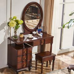 a dressing table with mirror, stool and flowers on it in front of a window