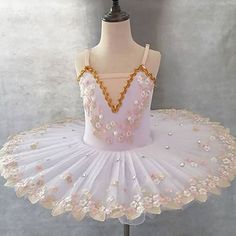 a white ballet dress with pink flowers on the bottom and gold trimmings, sitting on a mannequin