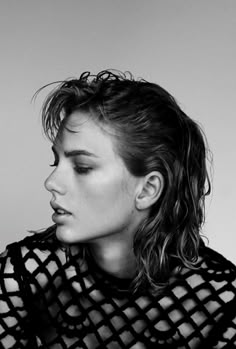 a black and white photo of a woman with her hair blowing in the wind, wearing a fishnet top