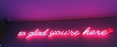 a neon sign that says so glad you're here on the wall above it