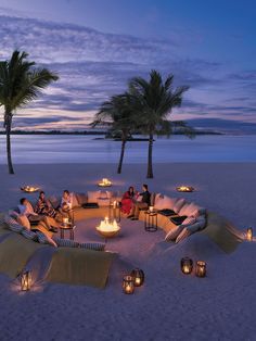 an image of people sitting around a fire pit on the beach with palm trees in the background