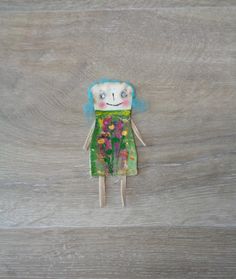 a doll with blue hair and green dress on wooden floor next to wood planks