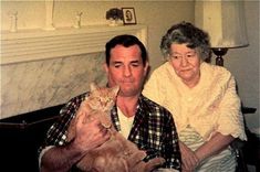 an older man and woman sitting next to each other holding a cat in their arms