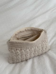 a crocheted purse sitting on top of a white bed next to a pillow