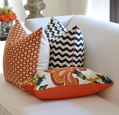 several pillows on a white couch in a room with orange and blue accents, including an orange flower