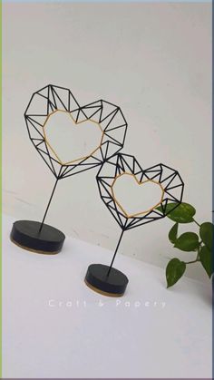 two heart shaped metal sculptures sitting on top of a white table next to a potted plant