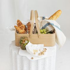 a basket filled with bread and grapes on top of a table next to a bag