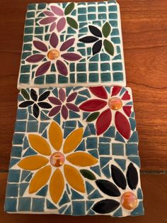 two colorful tiles with flowers on them sitting on a wooden table next to each other