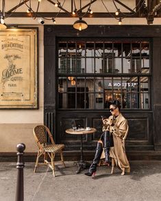 a woman sitting on a chair in front of a building with an old fashioned sign