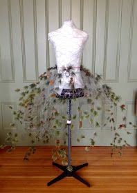 the mannequin is decorated with flowers and feathers on it's stand in front of a wall