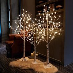 three lighted trees in the middle of a living room with fur rugs on the floor