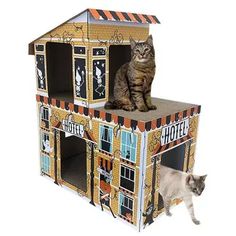 a cat is sitting on top of a cardboard doll house with another cat standing next to it