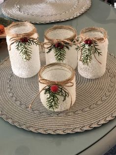 four mason jars decorated with pine branches and red berries are sitting on a placemat