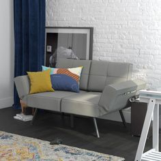 a grey couch with colorful pillows in front of a white brick wall and blue curtains