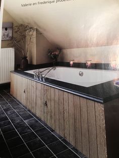 a bathroom with a large white bath tub next to a black tiled floor and wall