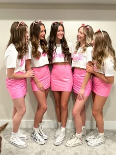 four girls in pink skirts and white shirts posing for the camera with their arms around each other