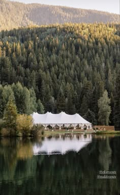 a large tent set up on the shore of a lake with trees in the background