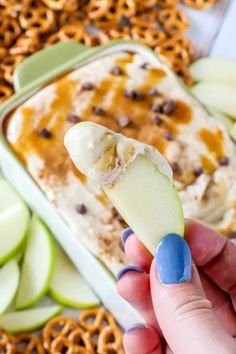 a hand holding an apple slice with pretzels and caramel in the background