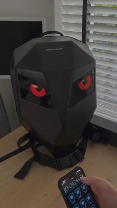 a person holding a remote control in front of a robot head with red eyes on it