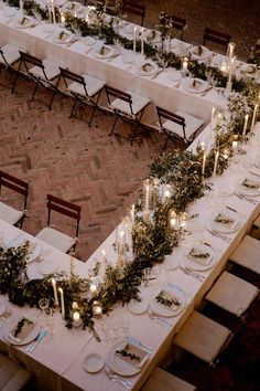 an overhead view of a long table with candles and greenery on it, surrounded by chairs