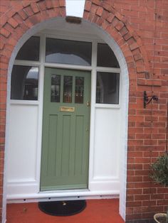 a green front door on a brick building with an arched glass window and white trim