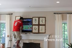 a man standing on a stepladder in front of a tv above a fireplace