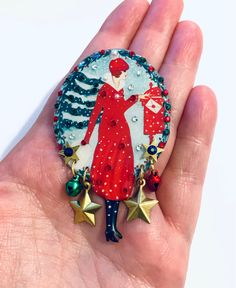 a hand is holding a brooch with a woman in red dress and stars on it