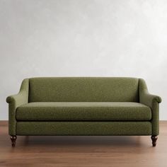 a green couch sitting on top of a hard wood floor next to a white wall