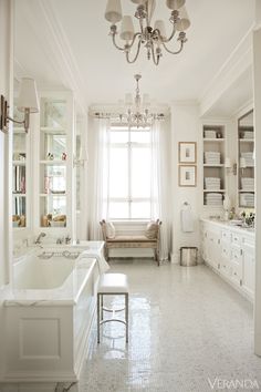 a white bathroom with a tub, sink and chandelier hanging from the ceiling