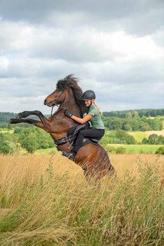 a woman riding on the back of a brown horse in a field with tall grass