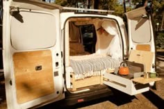 an open white van parked in the woods with it's door open and its bed pulled out