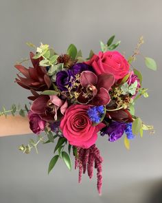 a bouquet of flowers is being held by someone's hand in front of a gray background