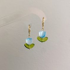 a pair of blue and green flower earrings hanging from gold earwires on a white background