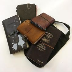 several different types of notebooks and books on a white table with a black bag