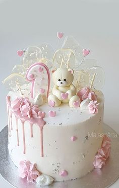 a white cake with pink decorations and a teddy bear sitting on it's top