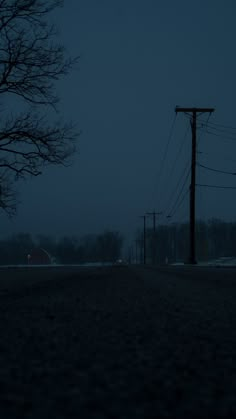 an empty street at night with power lines and telephone poles in the foreground on a dark, overcast day