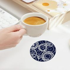 a person holding a cup of coffee in front of a keyboard and mouse on a desk